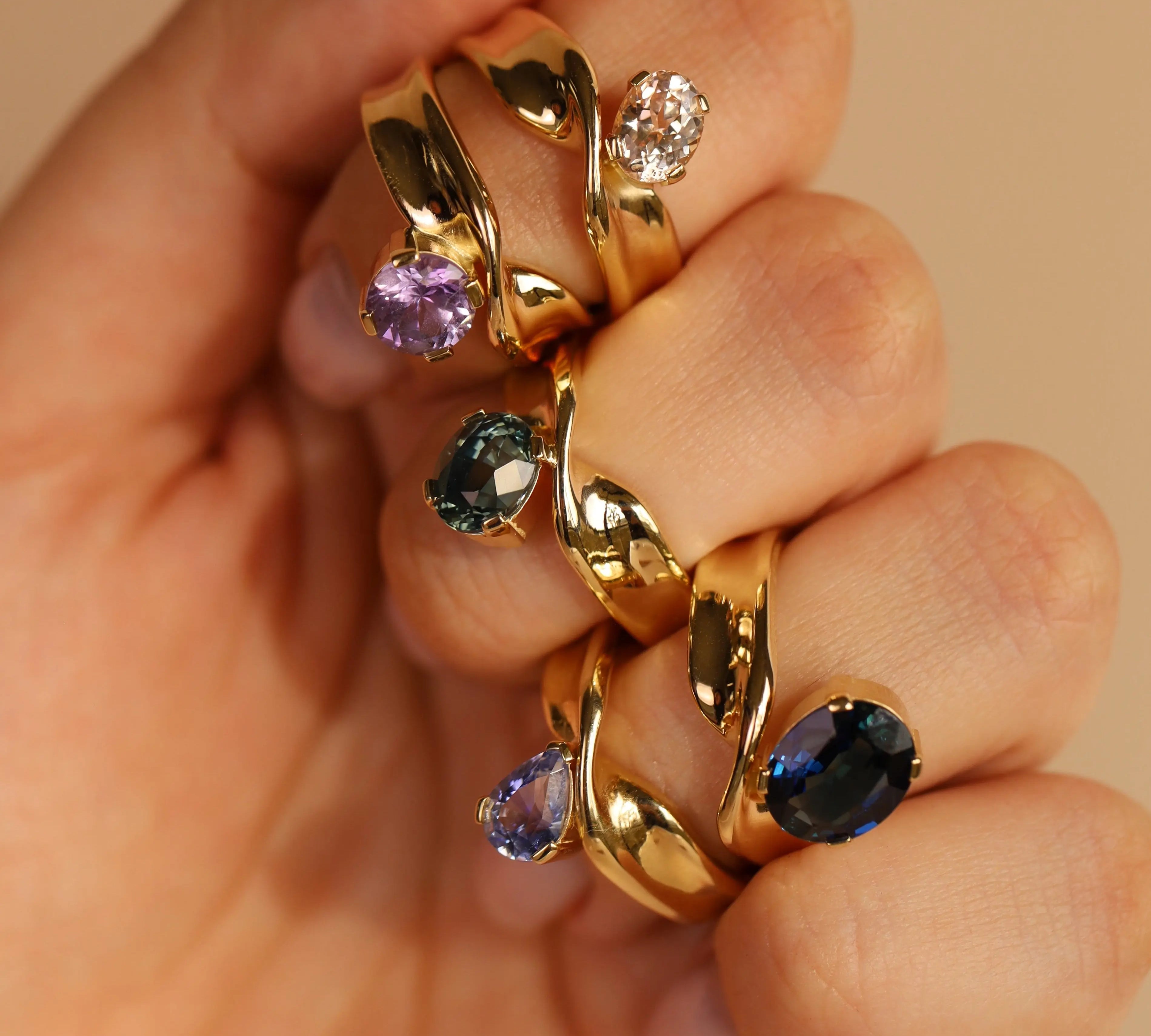 Gold rings with gemstones on a hand against a beige background