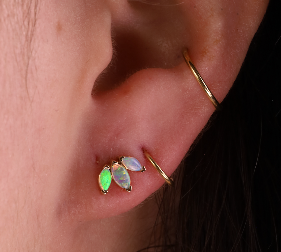 Close-up of an ear with gold earrings featuring green and opal stones.