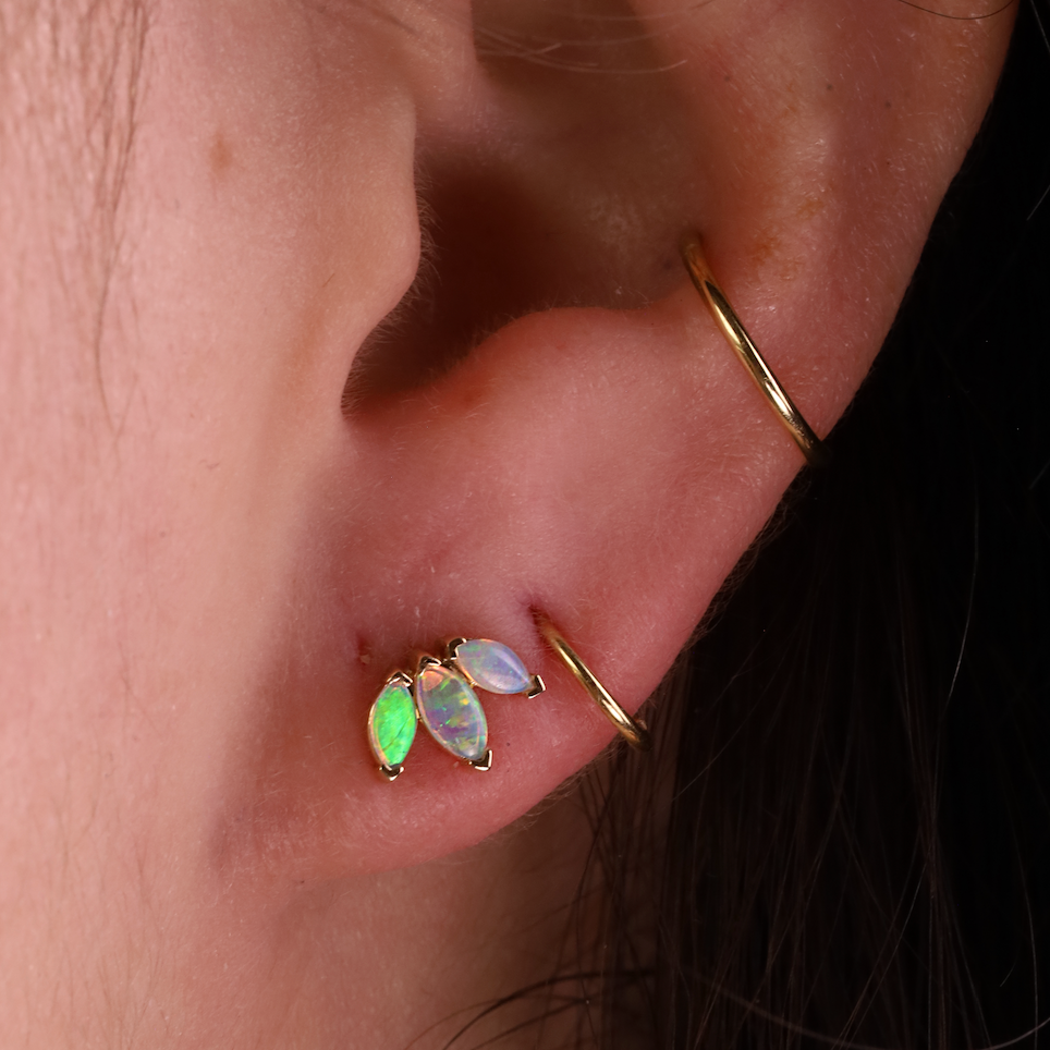 Close-up of an ear with gold earrings featuring green and opal stones.