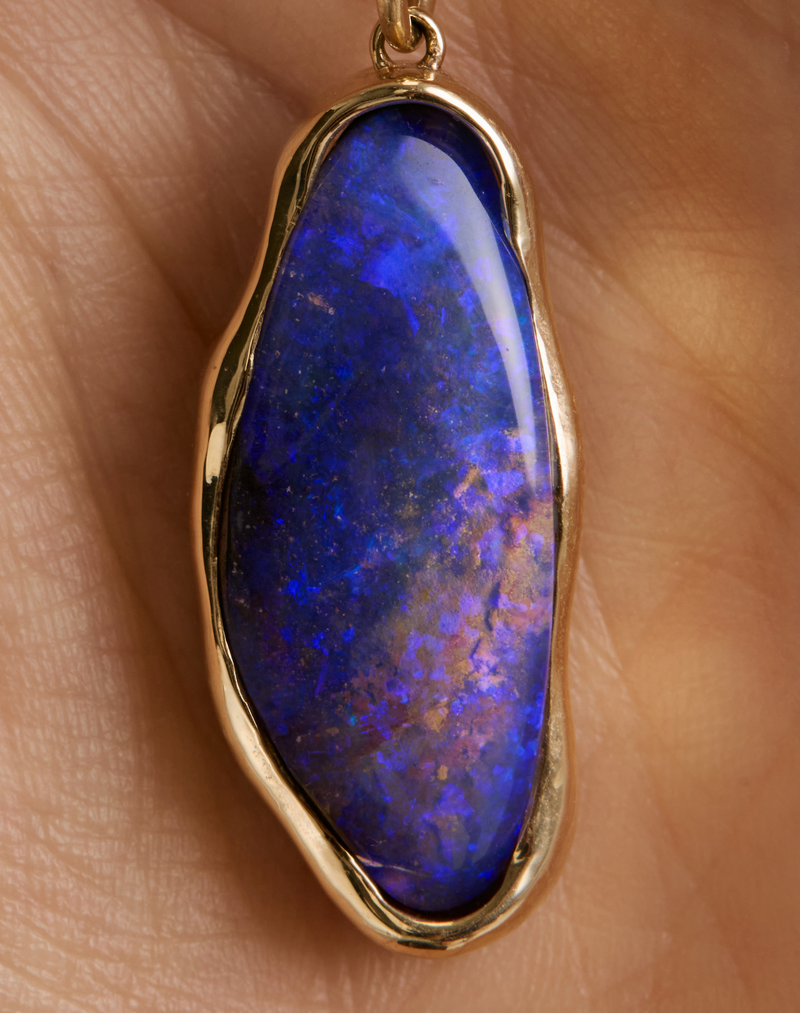 A close-up of a gold pendant with an irregularly shaped, vibrant blue opal gemstone, resting on a person's skin.