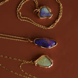 Three gold necklaces with opal pendants on a brown background