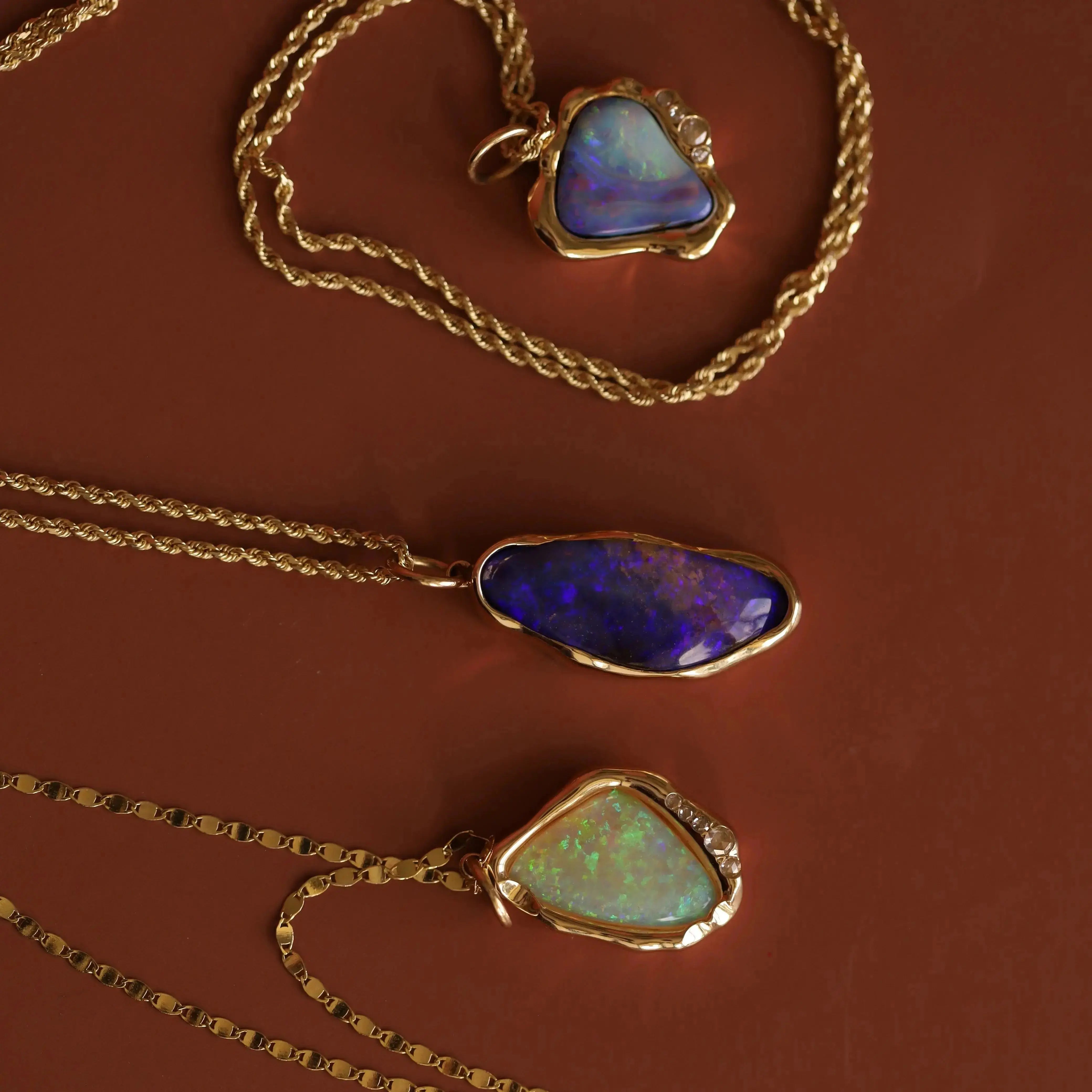 Three gold necklaces with opal pendants on a brown background