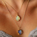 Two gold necklaces with opal pendants on a person's neck.
