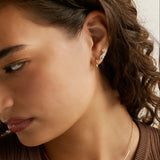 Close-up of a woman wearing a delicate gold chain necklace with a small clear stone pendant and matching gold hoop earrings with small clear stones.