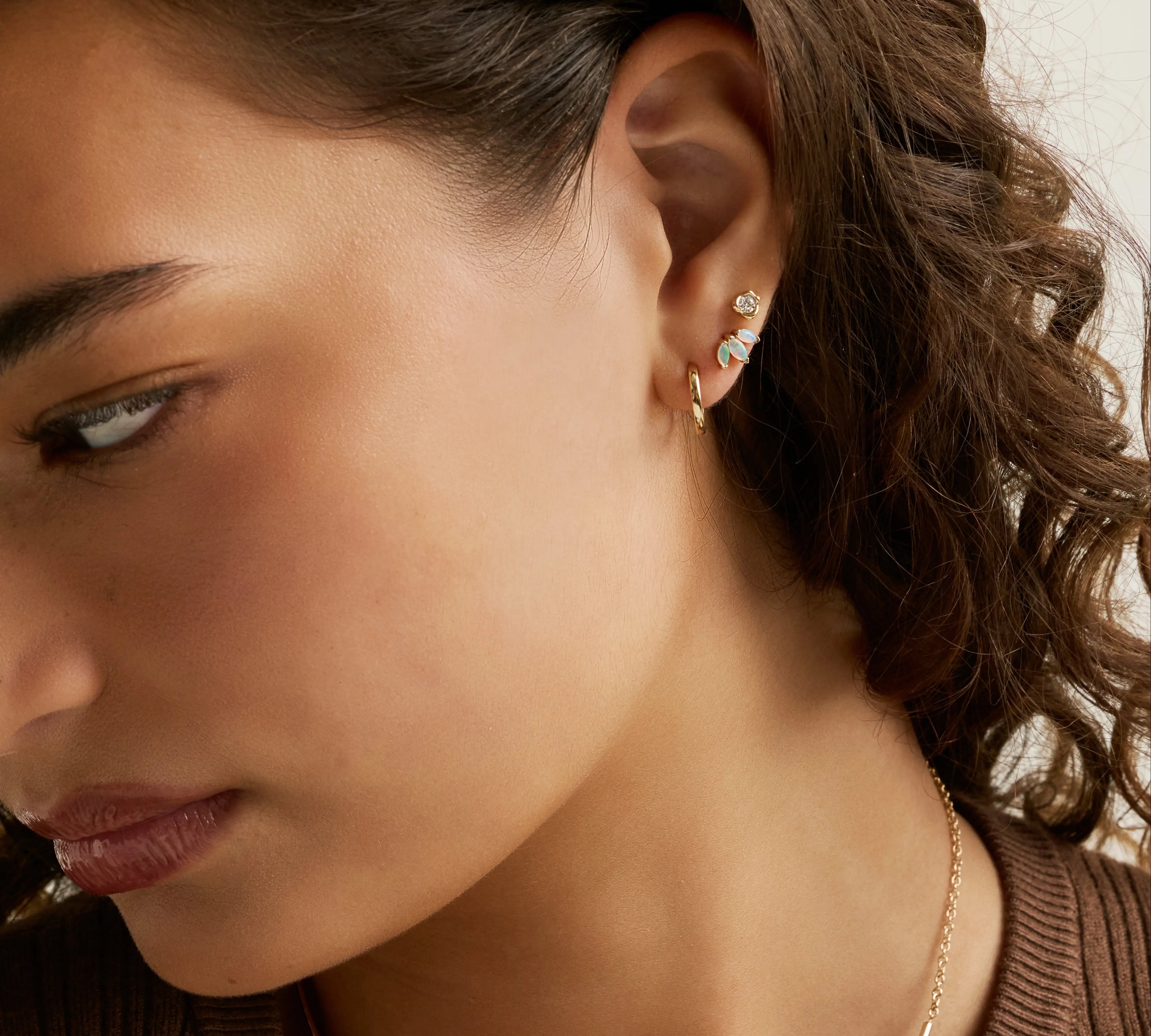 Close-up of a woman wearing a delicate gold chain necklace with a small clear stone pendant and matching gold hoop earrings with small clear stones.