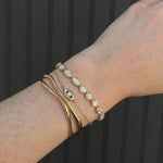Video of Lisse Tennis Bracelet, Solana Evil Eye Bracelet, and Curved Freeform Gold Cuff Bracelet on a woman's wrist against a black paneled wall 