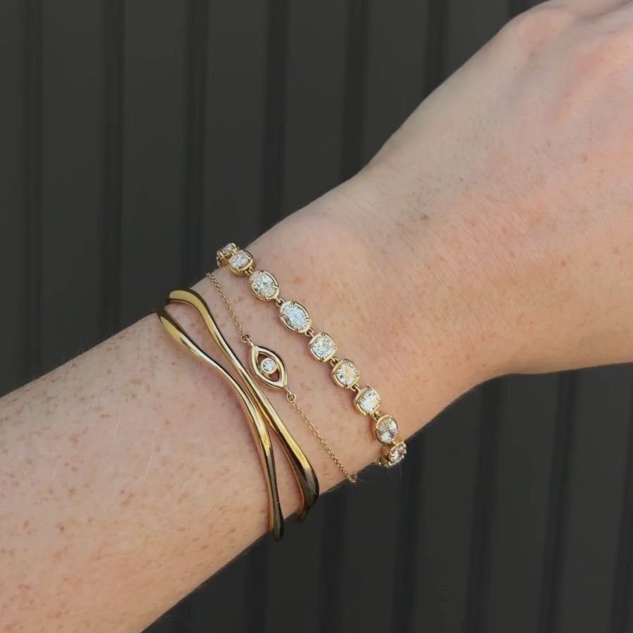 Video of Lisse Tennis Bracelet, Solana Evil Eye Bracelet, and Curved Freeform Gold Cuff Bracelet on a woman's wrist against a black paneled wall 