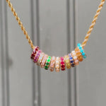 video of different color birthstone rondelles on a gold chain against a dark wall background