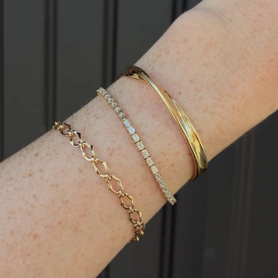 Video of Mini Twist Link Cuff, Evert Tennis Bracelet, 8mm Sculpted Link Gold Chain Bracelet on woman's wrist, against a black paneled wall