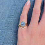 Video of gold Forget Me Not Cameo ring (featuring a carved blue flower) on pinky, stacked with a wavy diamond band, shown against a denim background.