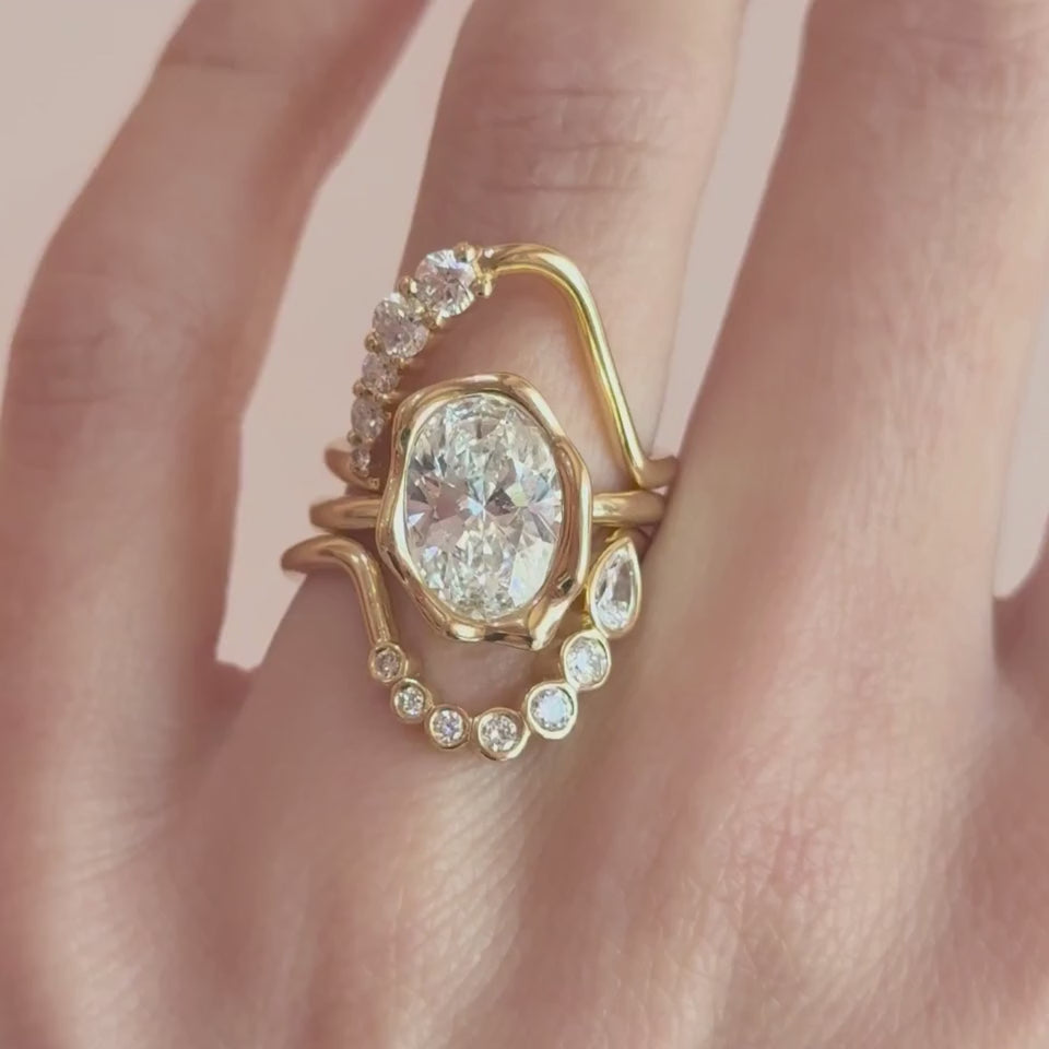 Video of The Abstract Bezel Oval Engagement Ring framed by two White Diamond Lucy Wave Bands on hand