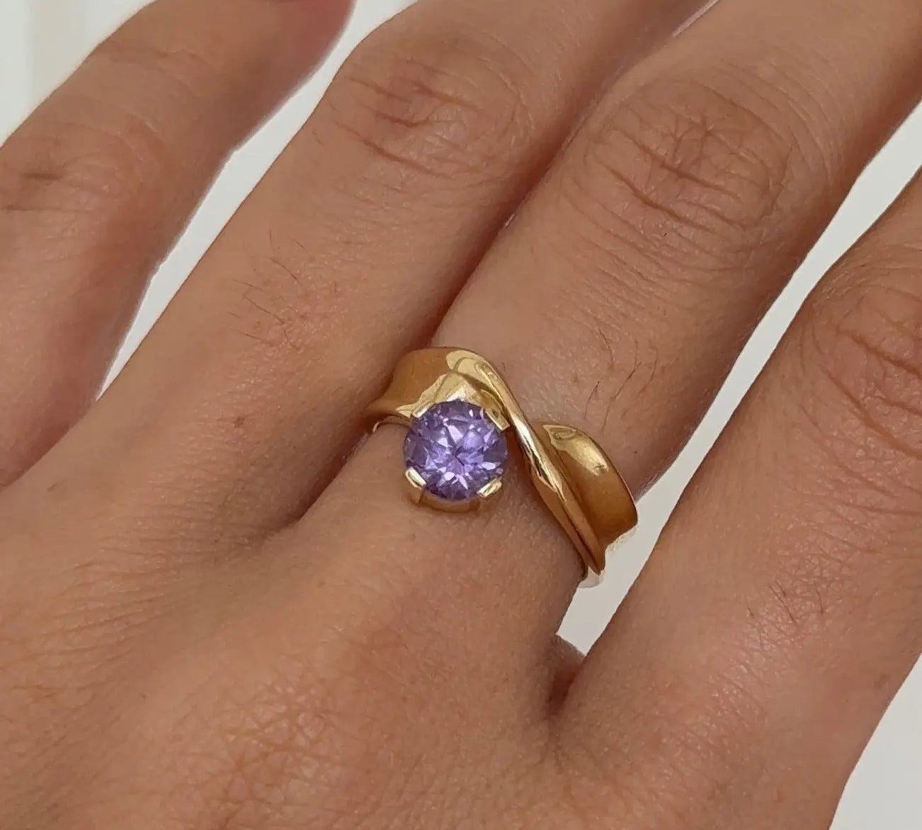 Gold ring with a purple gemstone on a hand against a white background
