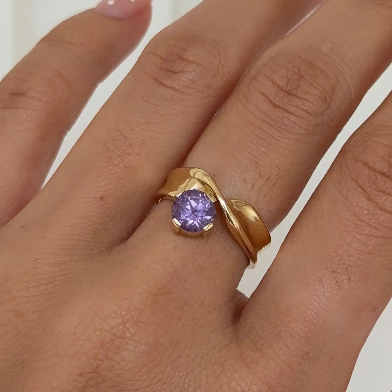 Gold ring with a purple gemstone on a hand against a white background