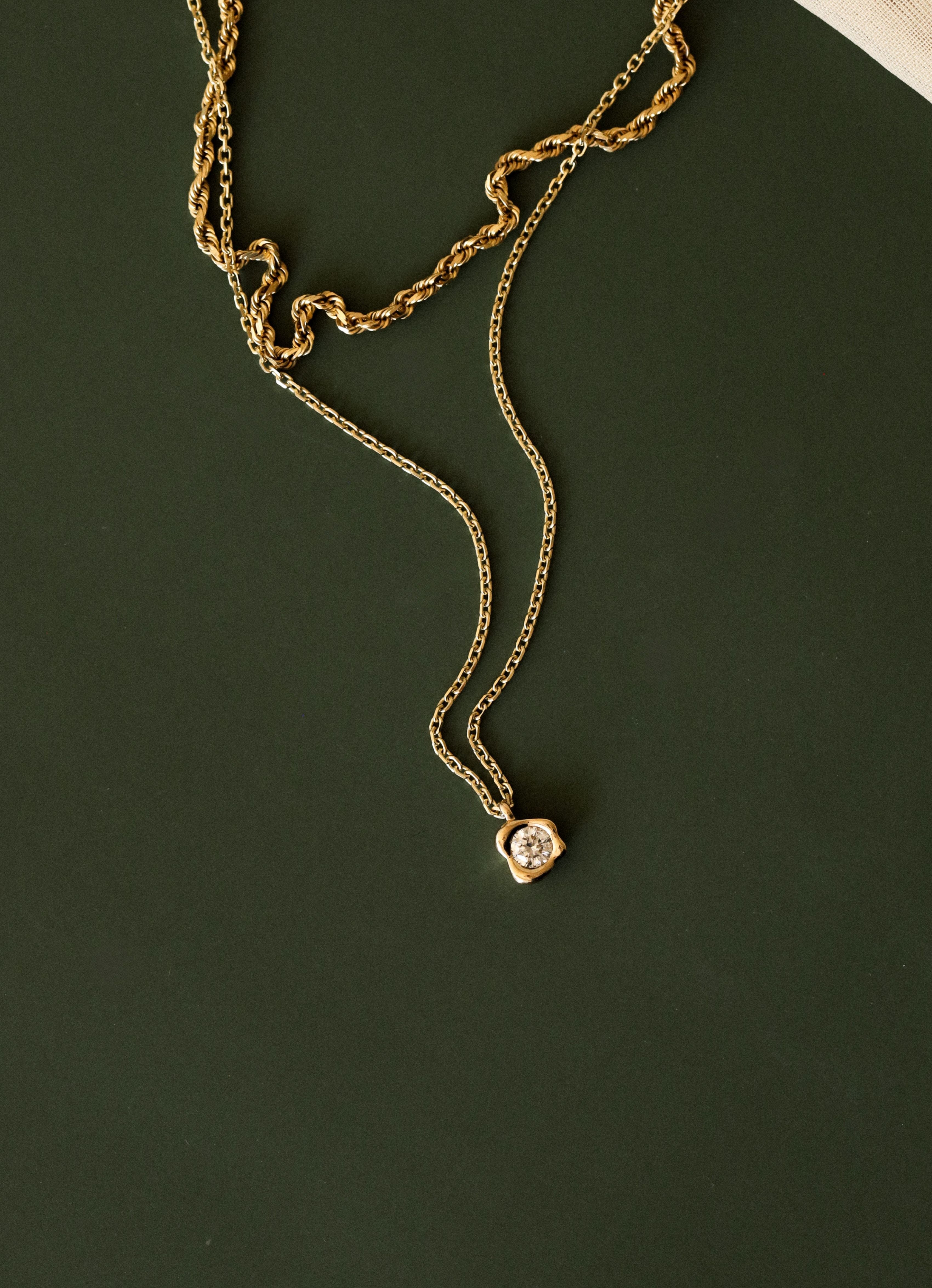 Gold necklace with a small pendant on a dark green background