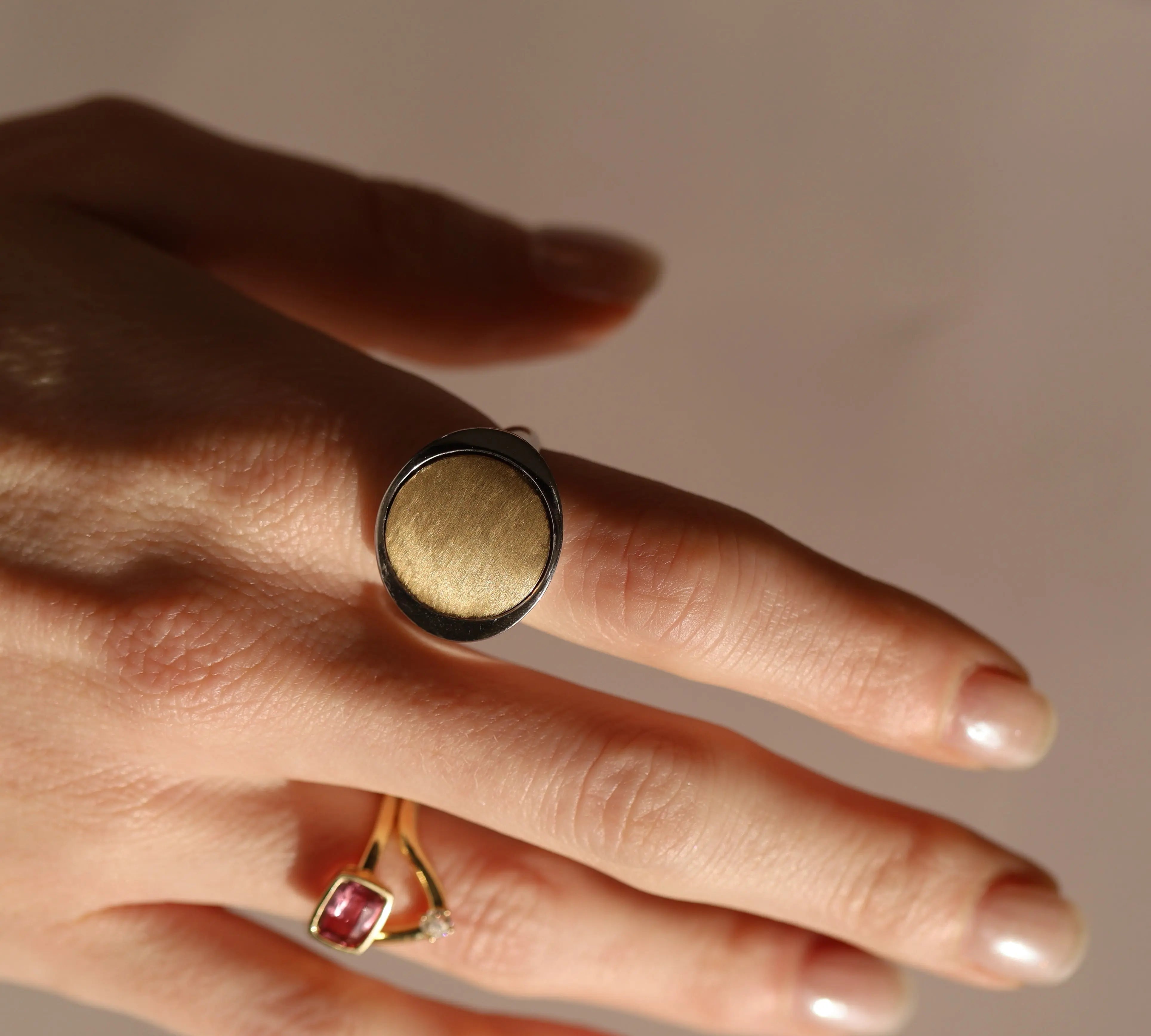 Hand wearing a gold ring with a red gemstone on a neutral background