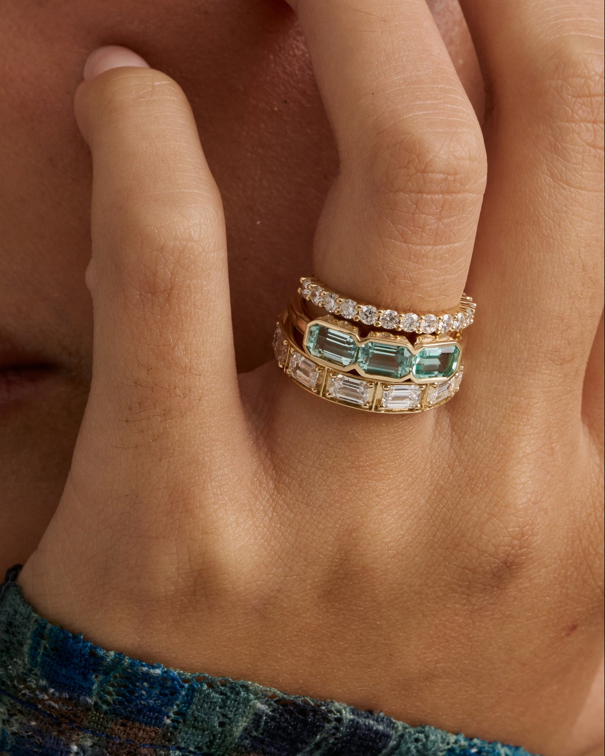 Hand wearing stacked diamond bands with baguette and emerald cut diamonds, resting on tweed