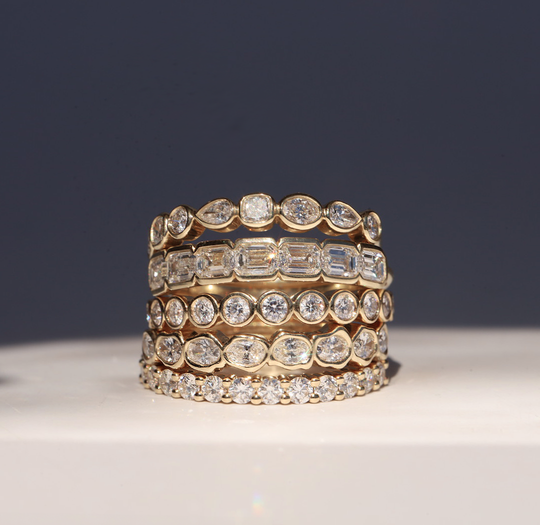 Stack of white diamond stacking bands with bezel-set mixed-shape diamonds on a white pedestal