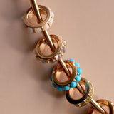 close up of circular charms with birthstones around on a neutral pink background