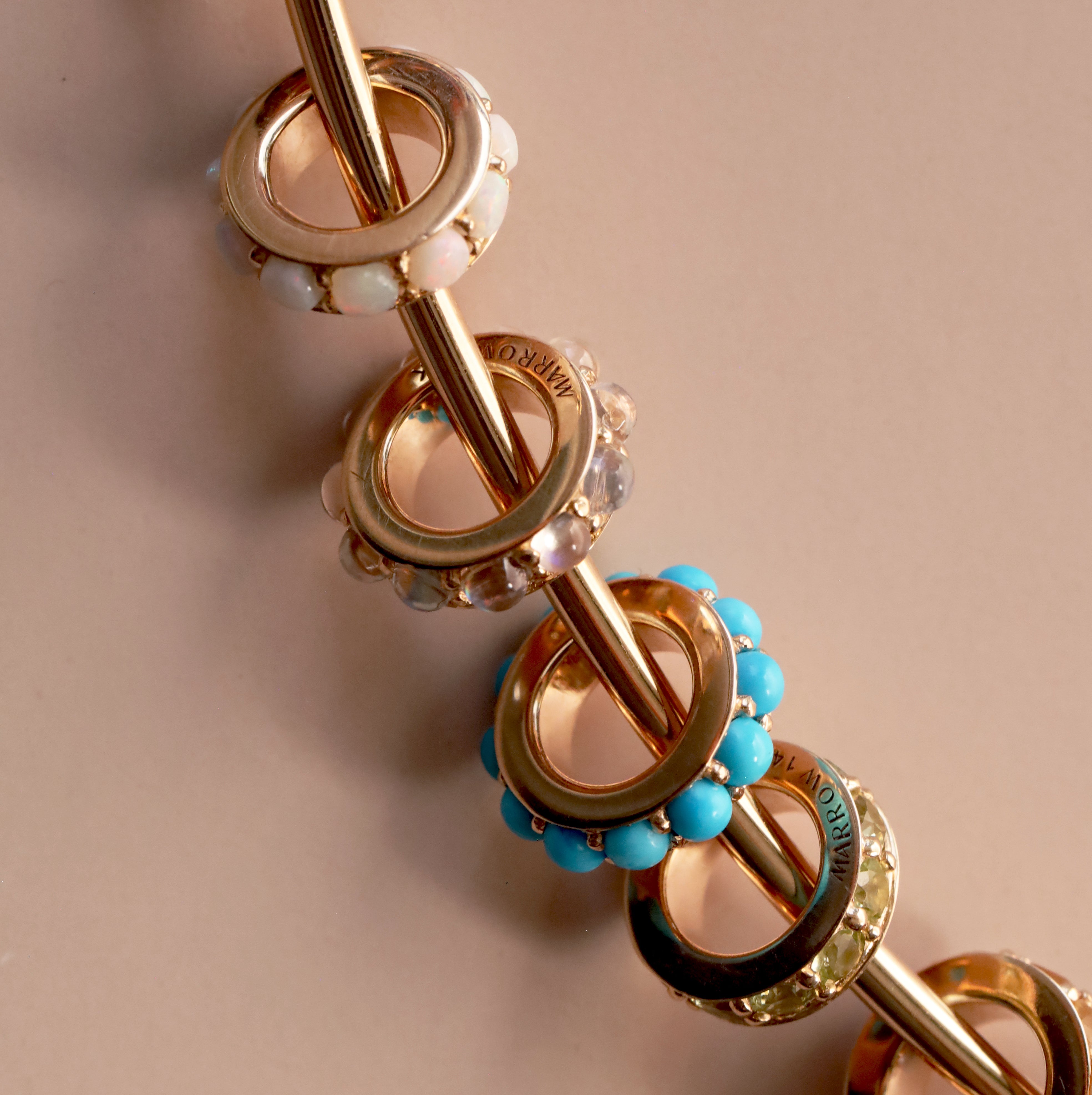 close up of circular charms with birthstones around on a neutral pink background