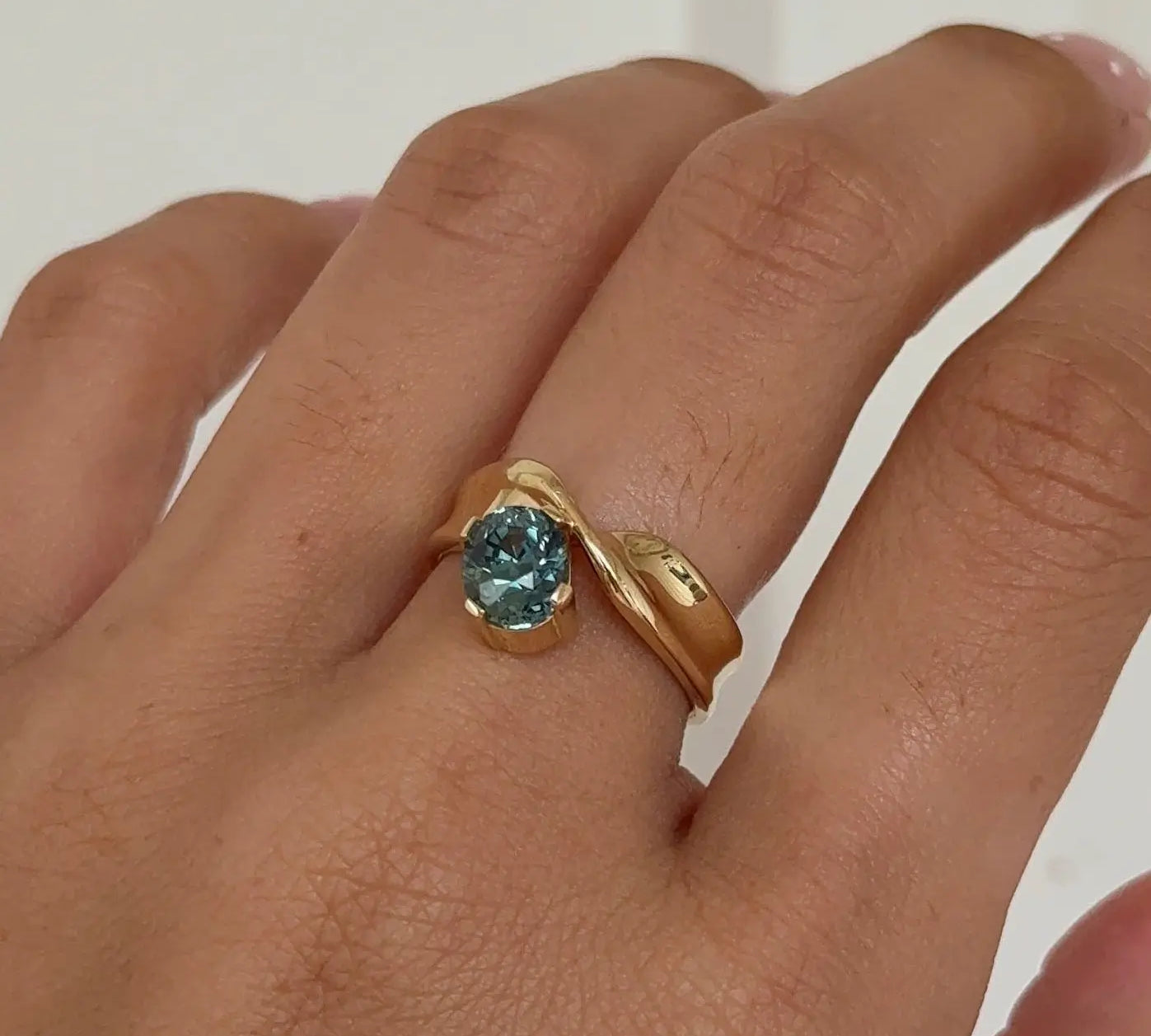 Hand wearing a gold ring with a blue gemstone on a plain background