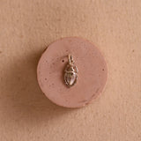 Silver scarab charm on a pink ceramic circular pedestal against a neutral fabric background