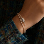 close up of woman's wrist with a dainty diamond tennis bracelet and a silver bracelet with a scarab 