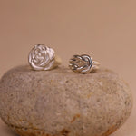 Two silver rings, one rose-shaped and one knot-shaped, on a stone surface with a beige background.