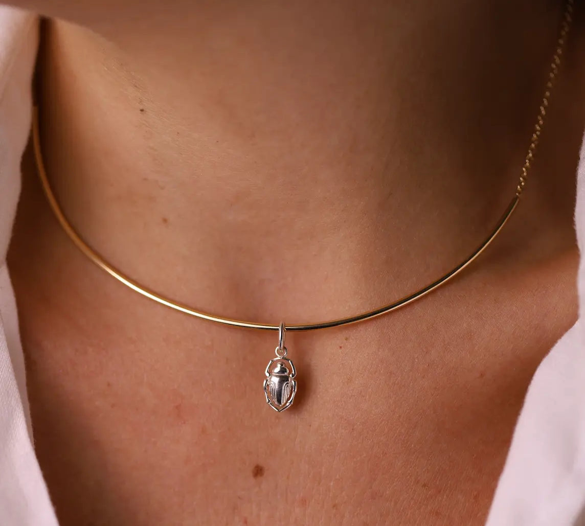 Gold necklace with a silver pendant on a person wearing a white shirt.