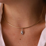Gold necklace with a silver pendant on a person wearing a white shirt.