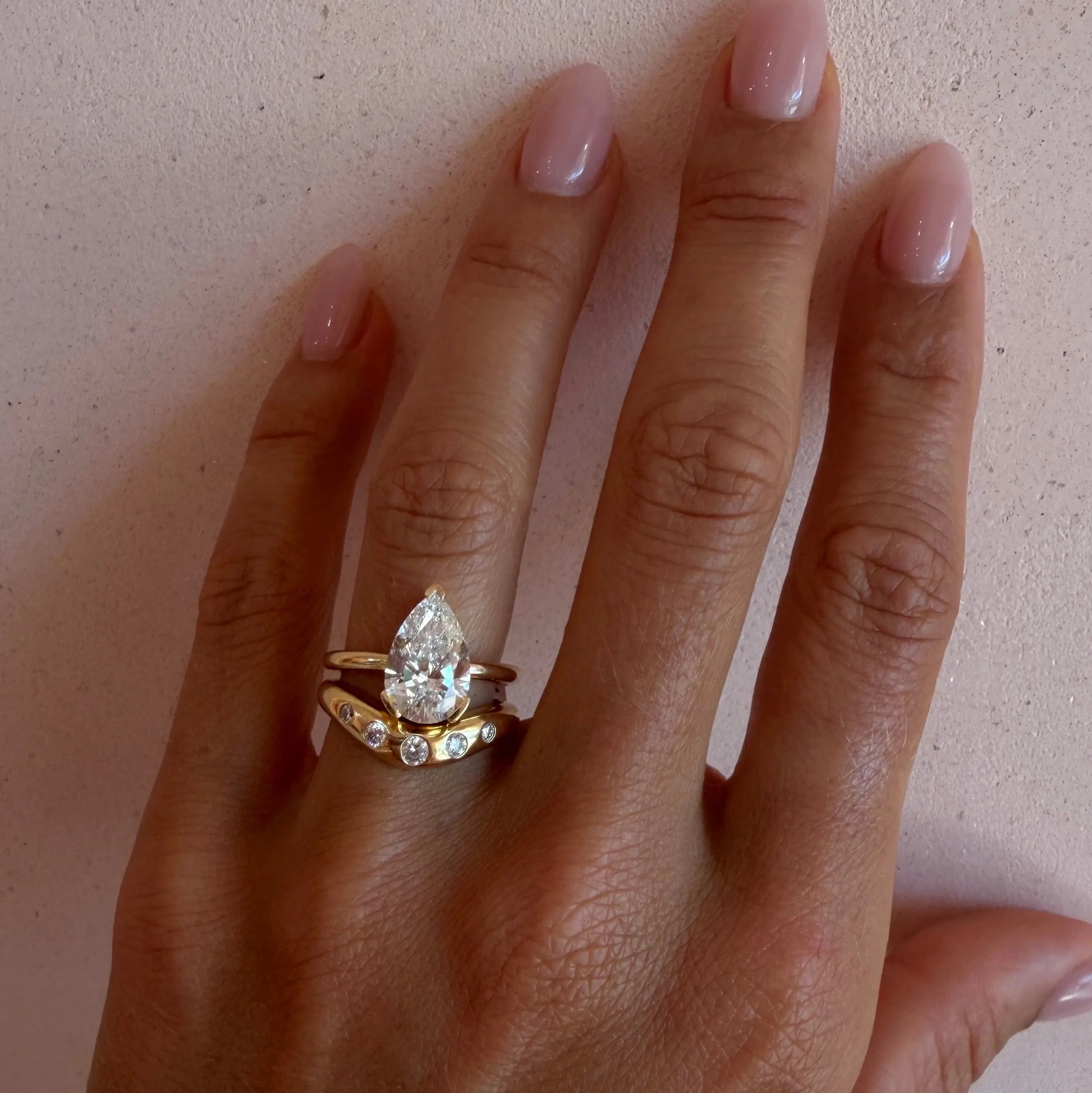 The Sloane Pear Solitaire Engagement Ring stacked with the White Diamond Bombé Band on hand