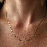 Close-up of a person wearing a gold necklace on a neutral background
