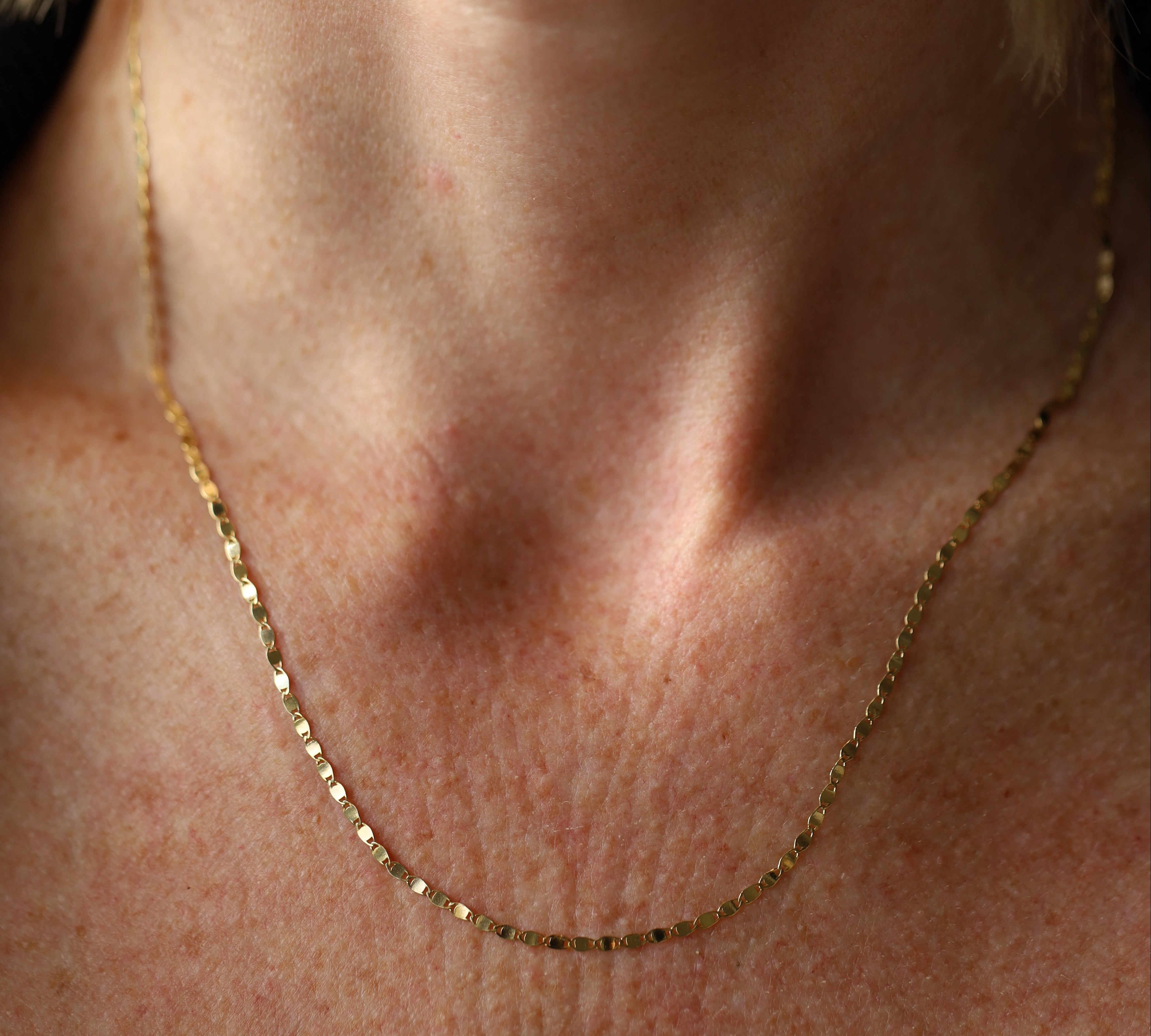 Close-up of a person wearing a gold necklace on a neutral background