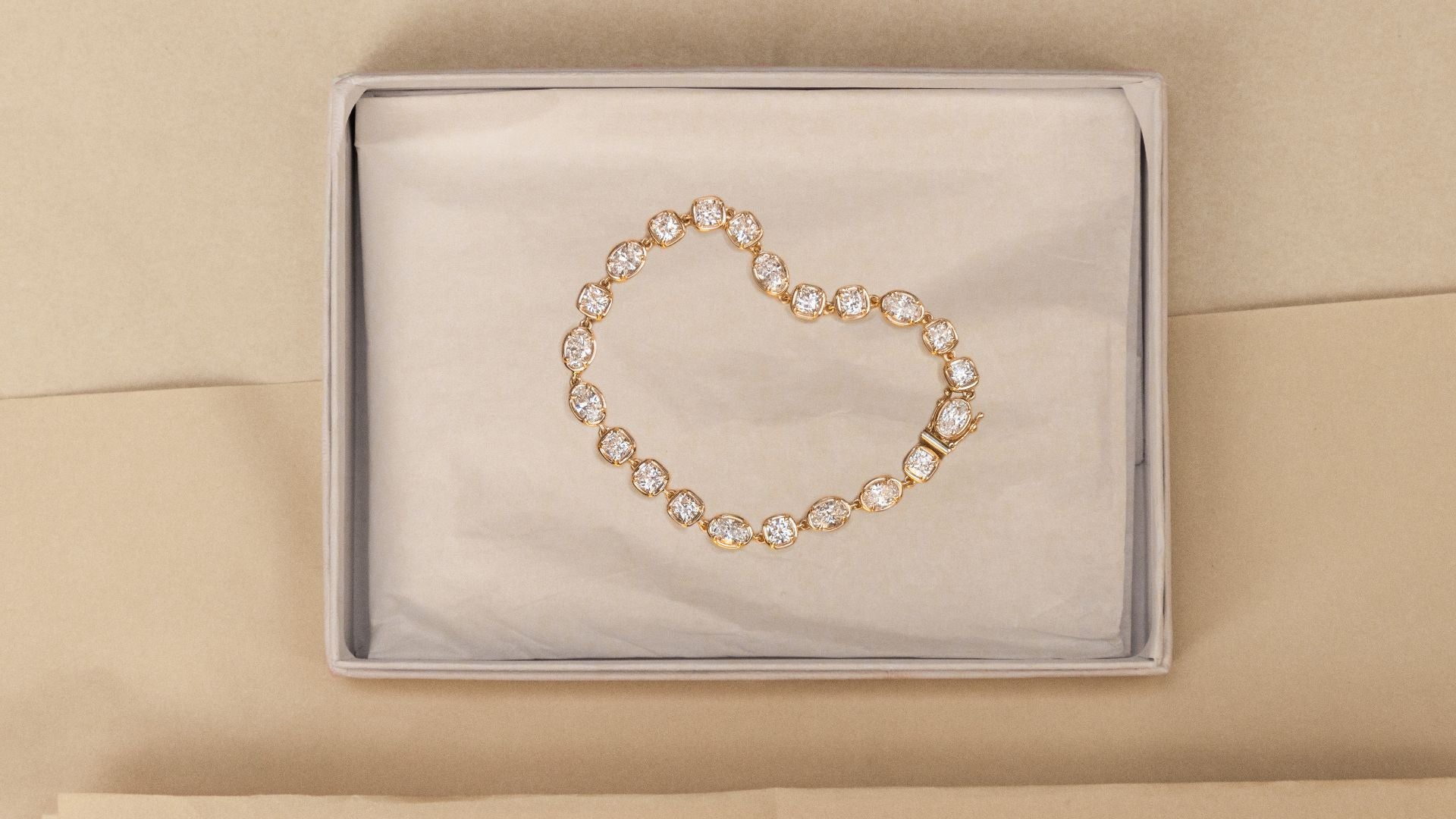 flat lay of mixed-shape diamond tennis bracelet laid on an open neutral white/gray box on a beige background