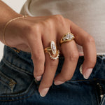 close up of woman's hand resting against top of denim wearing multiple yellow gold and diamond rings stacked together.